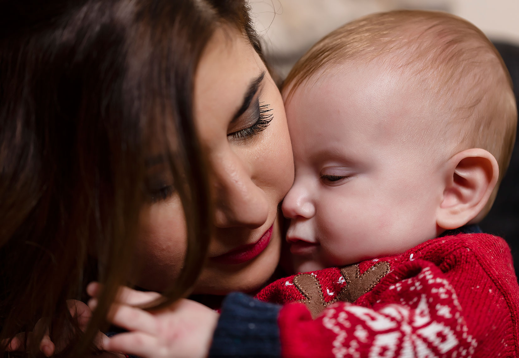 Young mother with brown hair gently holding baby wearing red sweater