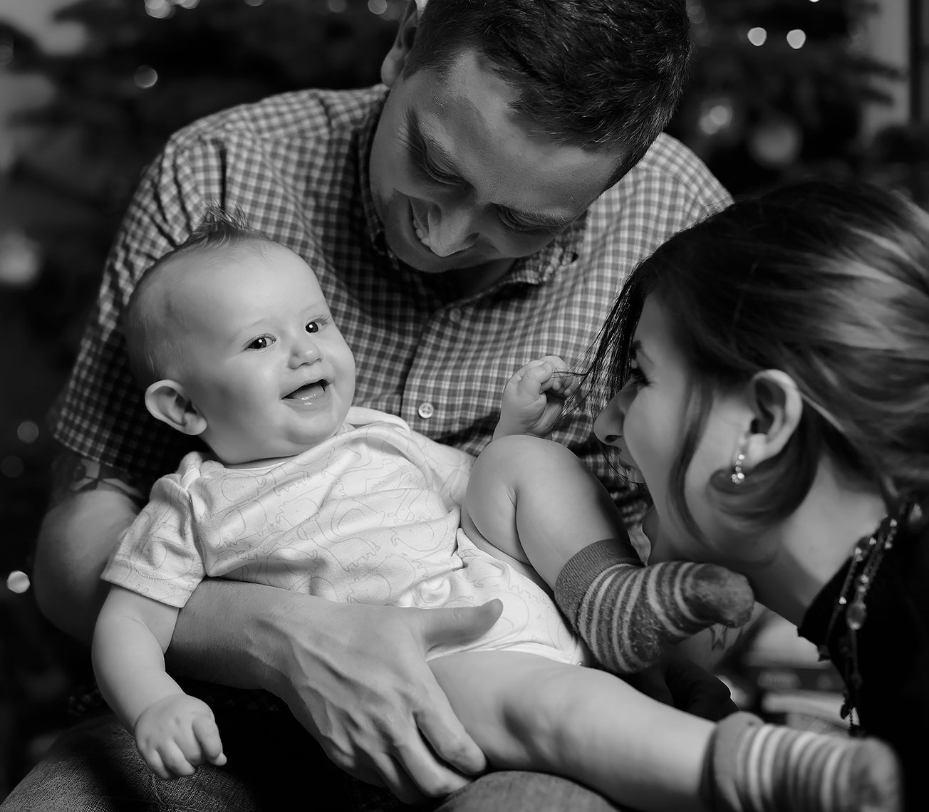 Young pretty woman with dark hair smiling at laughing baby being held by young man
