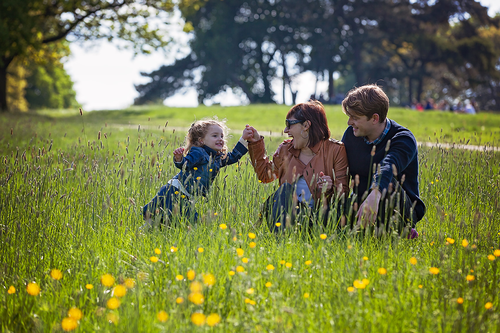 Family lifestyle portrait of young woman with young daughter and man in green fields during summer