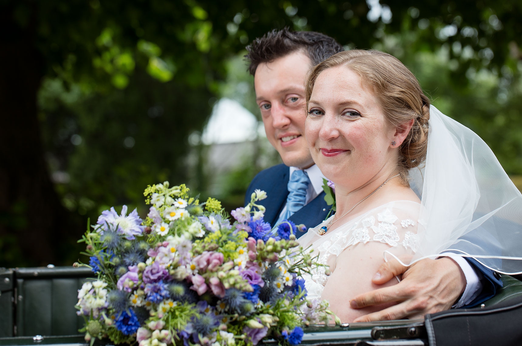 Bride and Groom cuddling in vintage car with bouquet of flowers