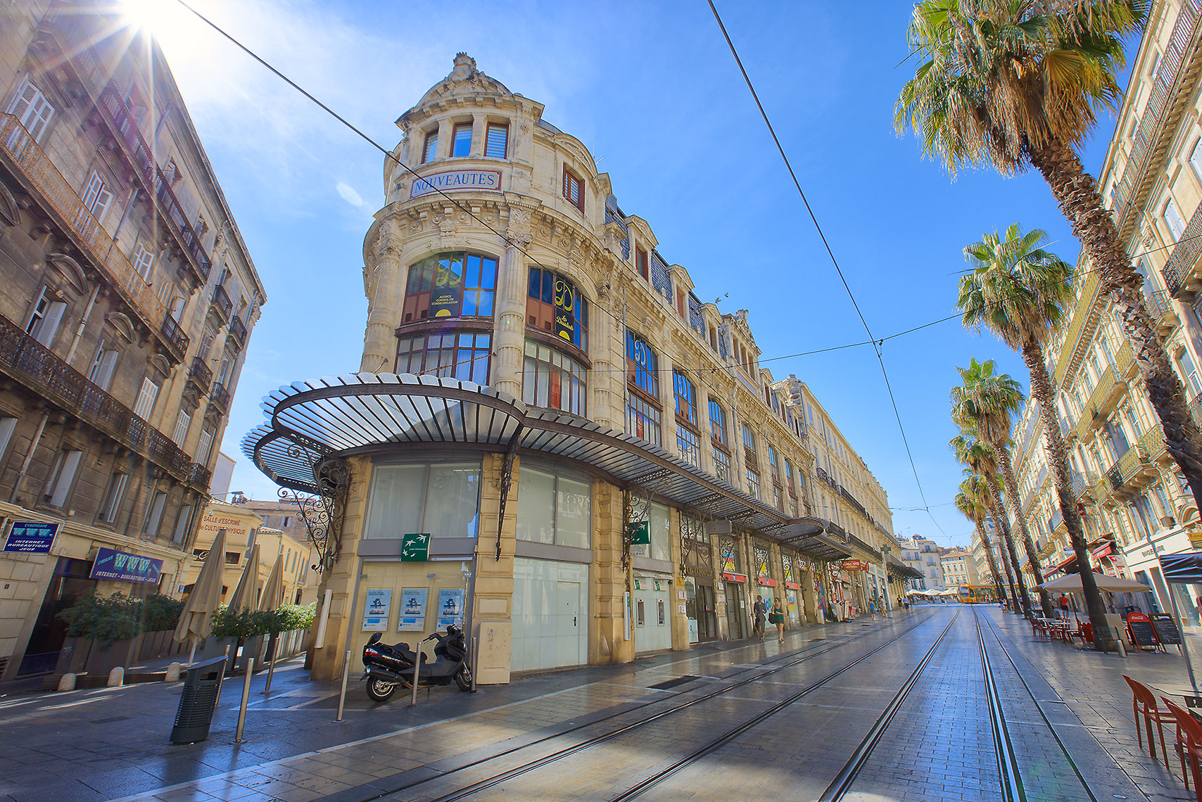 French Architecture with yellow buildings and cobble-stoned street and tram line with sun rising over buildings