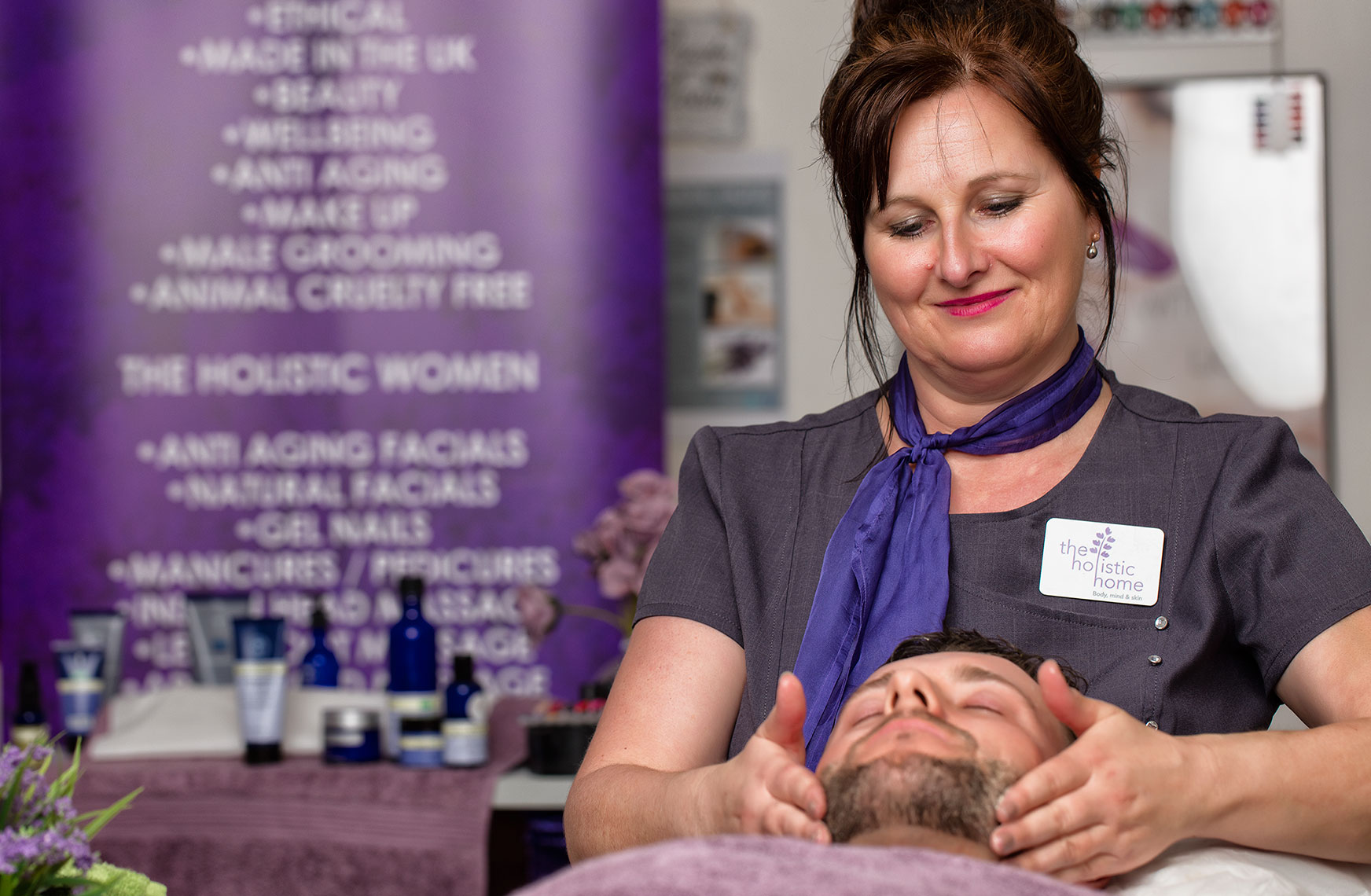 Middle-aged female massage therapist in purple giving a facial to a handsome young bearded man