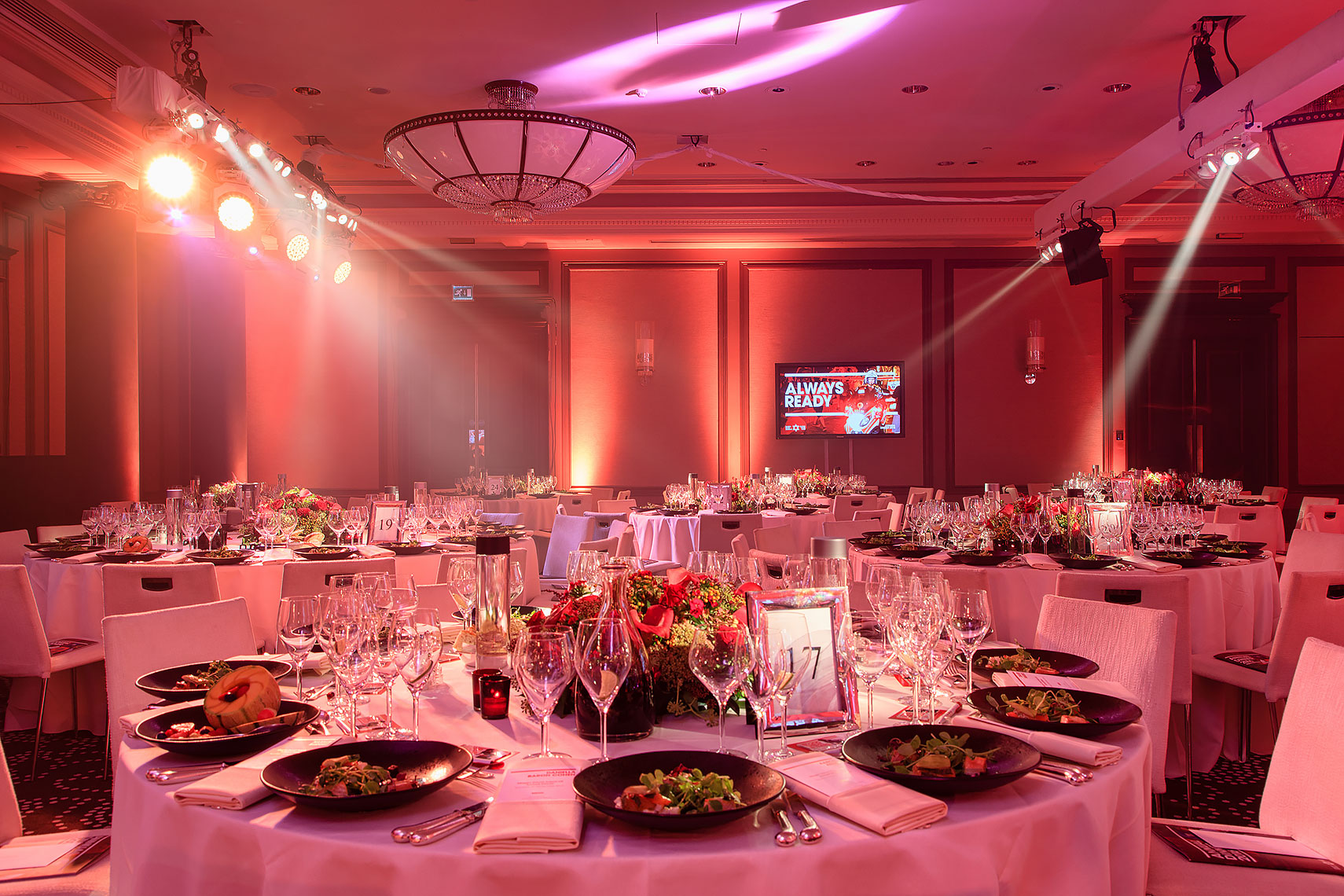 Colourful ballroom set for fancy evening event with flowers and decorations under red lighting